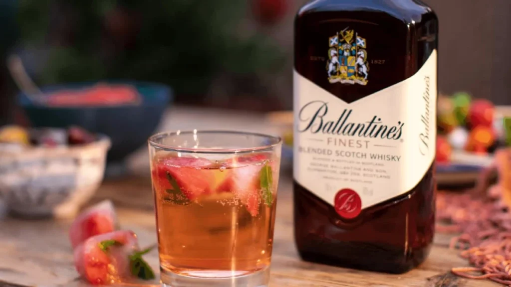 Garrafa de Ballantine's Finest ao lado de um copo de whisky com gelo e frutas.