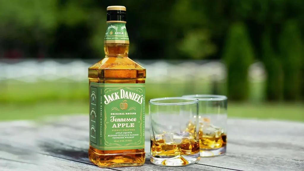 Garrafa de Whisky Jack Daniel's Tennessee Apple com dois copos de whisky com gelo sobre uma mesa ao ar livre.