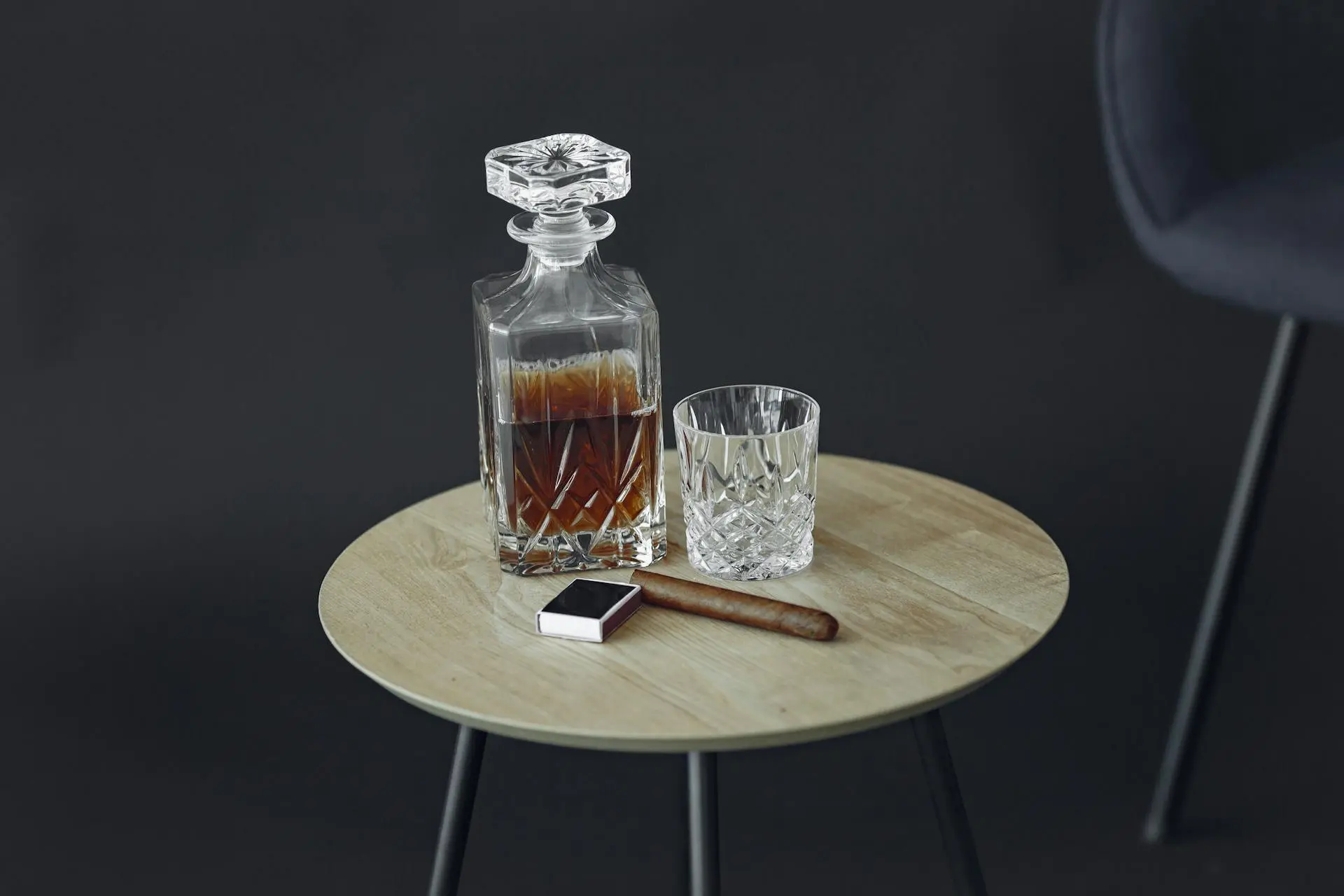 Garrafa de cristal com whisky e copo ao lado de um charuto em uma mesa, ideal para quem busca qual o melhor whisky.