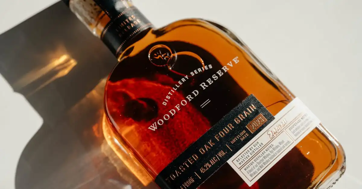 Garrafa de whisky Woodford Reserve sobre uma superfície, destacando sua elegância e tom dourado.