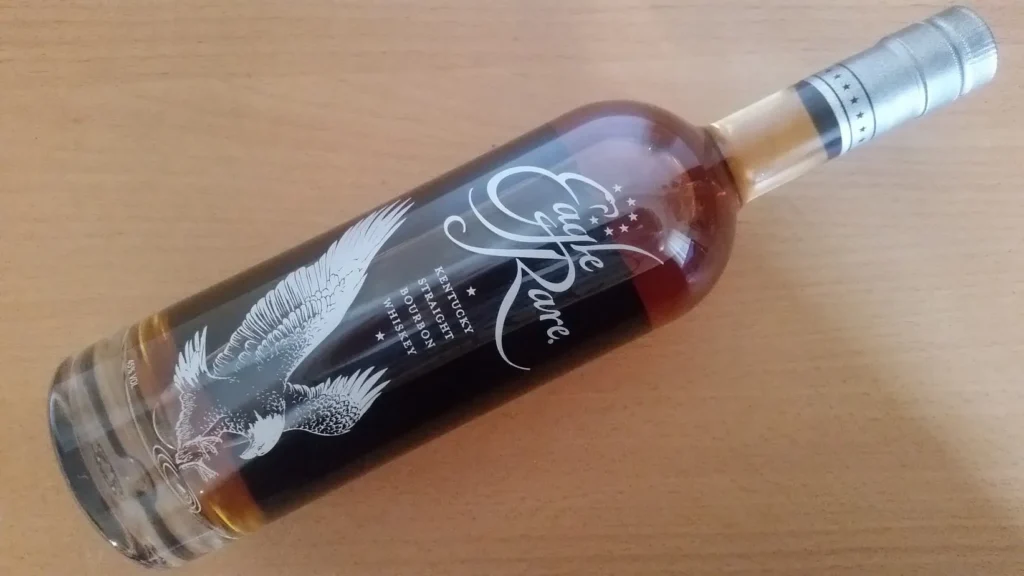 Garrafa de Whisky Eagle Rare deitada sobre uma mesa de madeira, destacando sua elegância e tradição entre os bourbons.