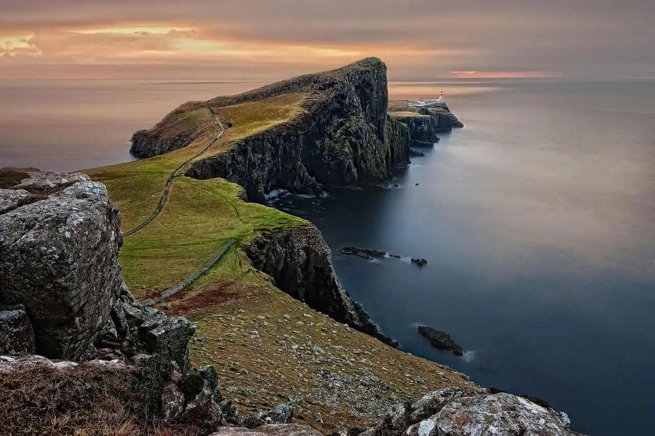 Paisagem costeira rochosa da Escócia próxima à destilaria do Whisky Talisker 10 Anos, com penhascos e farol ao fundo