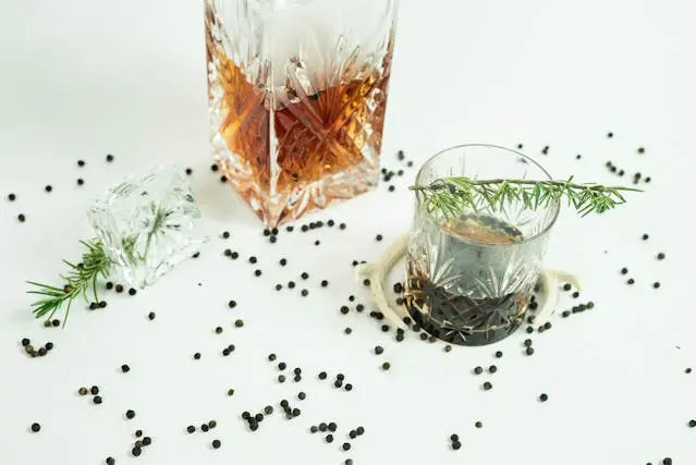 Um copo de whisky Talisker com raminho de alecrim, pimenta em grãos e um cubo de gelo