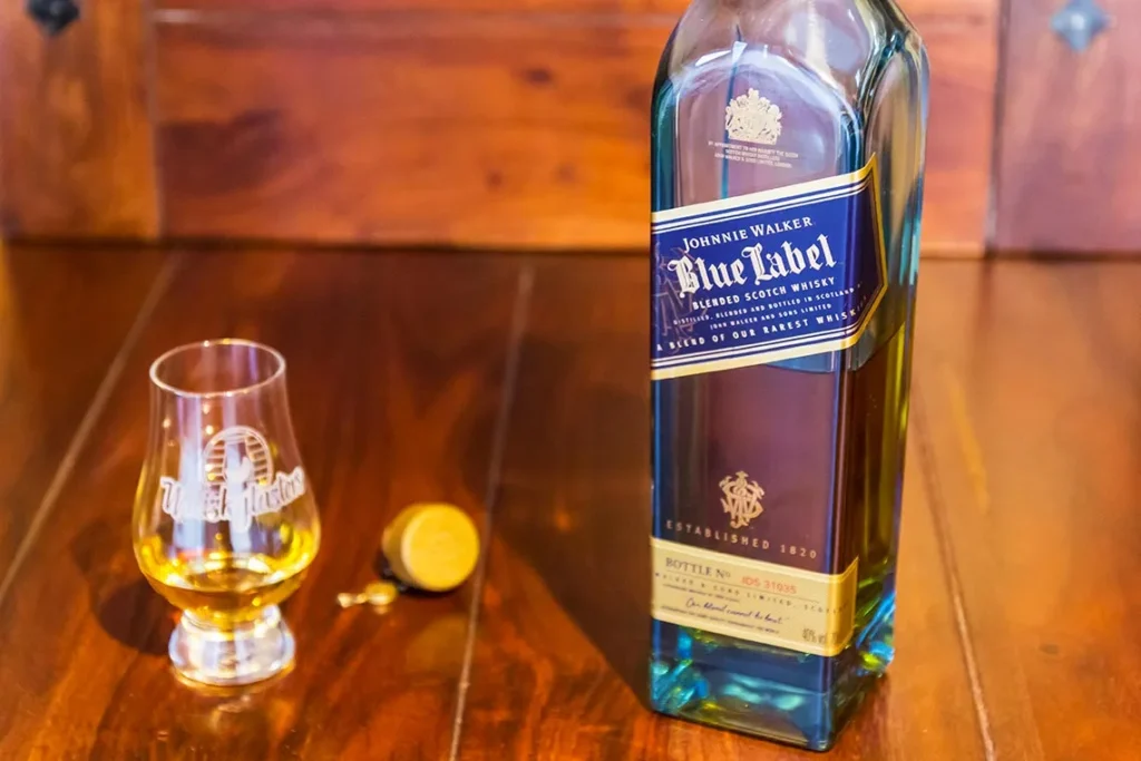 Garrafa de Johnnie Walker Blue Label com taça de whisky sobre mesa de madeira